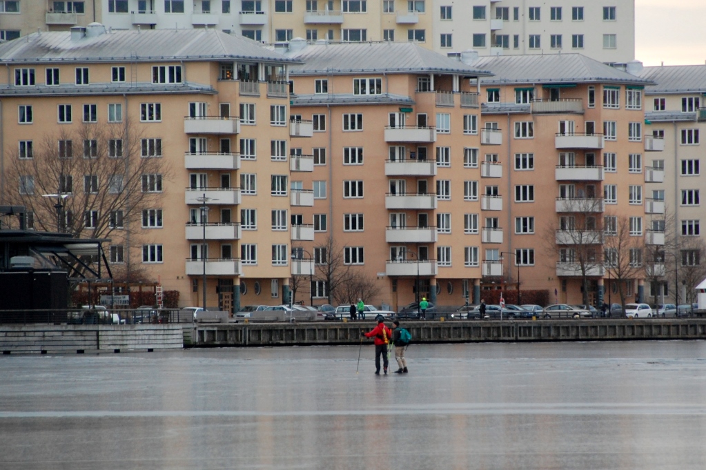 Vissa skridskoåkare åker nära husbåtarna, men dessa håller sig närmare Hornsbergs strand på Kungsholmen (andra sidan vattnet)
